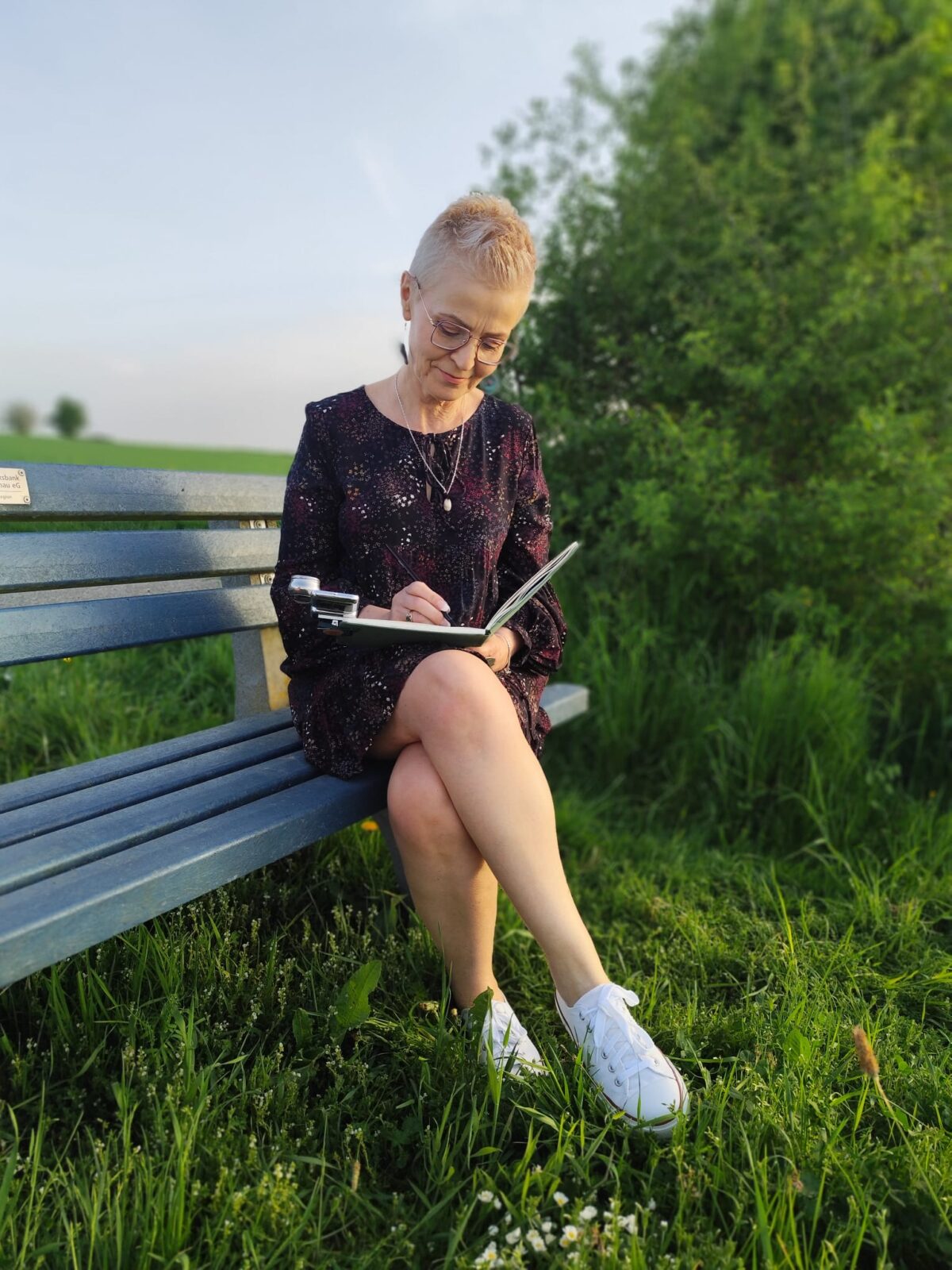 Monika Bargieł sitzt auf einer Bank im Grünen und skizziert konzentriert in ihr Notizbuch.